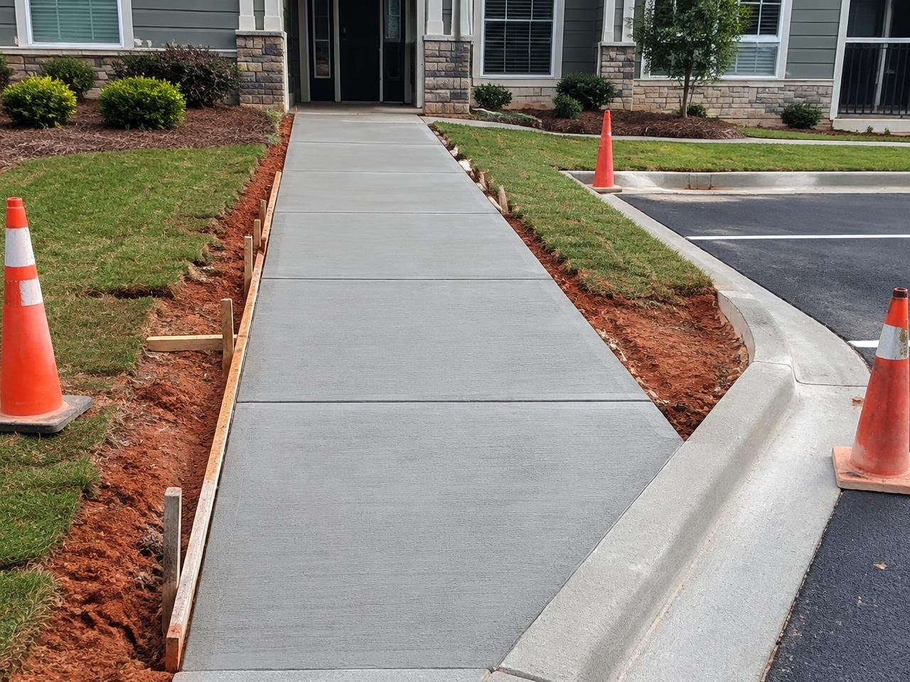 Freshly poured broom-finished concrete sidewalk with new curb at an apartment entry